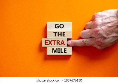 Go the extra mile symbol. Wooden blocks with words 'Go the extra mile'. Male hand. Beautiful orange background. Business and go the extra mile concept. Copy space. - Shutterstock ID 1889676130