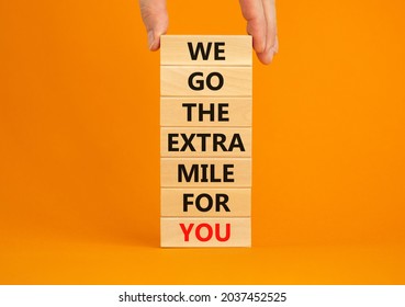 Go The Extra Mile Symbol. Wooden Blocks With Words 'We Go The Extra Mile For You'. Businessman Hand. Beautiful Orange Background. Business And Go The Extra Mile Concept. Copy Space.