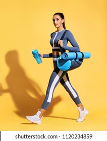 Go to gym! Attractive latin woman in fashionable sportswear on yellow background. Dynamic movement. Side view. Sports and healthy lifestyle