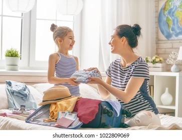 Go on an adventure! Happy family preparing for the journey. Mom and daughter are packing suitcases for the trip.