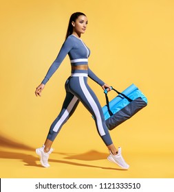 Go to training. Sporty woman with bag on yellow background. Dynamic movement. Side view. Sport and healthy lifestyle