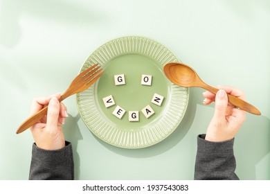 Go vegan diet, Green and Eco living concept. A set of plate and wooden spoon and fork with alphabet letter arranging into a word "Go Vegan" on green table with woman's hands hold a spoon and fork.