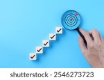 Goal Achievement Steps and Target Concept. Wooden blocks with checkmarks forming a staircase toward a magnifying glass highlighting a target, representing goal achievement and focus. business growth,