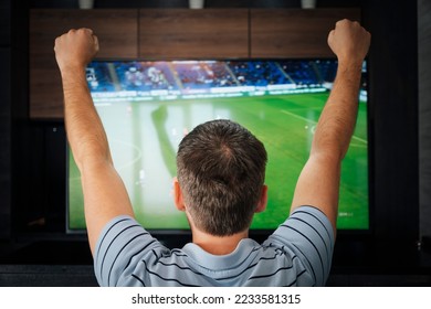 Goal. emotional fan watching football at night, view from the back. Man watching football match on television at home.