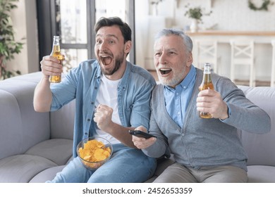 Goal! Excited football soccer baseball fans old father and adult son rooting cheering for favorite sport team watching match on TV drinking beer on sofa. Happy father`s day! - Powered by Shutterstock