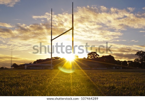 Goal posts for football, rugby union or league on\
field at sunset
