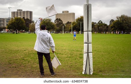 A Goal Umpire Waves Two White Flags At A Kid's Local Non Ticketed Australian Rules Football Game.