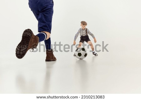 Goalkeeper. Boys, children in classical retro clothes playing football over grey studio background. Concept of game, childhood, friendship, activity, leisure time, retro style, fashion.