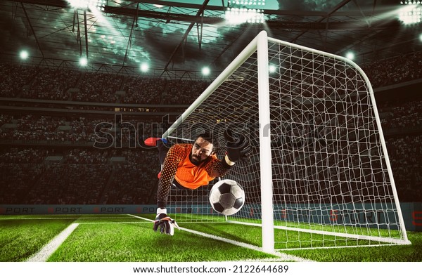 Goalkeeper in orange uniform catches the ball in the\
stadium during a football\
game