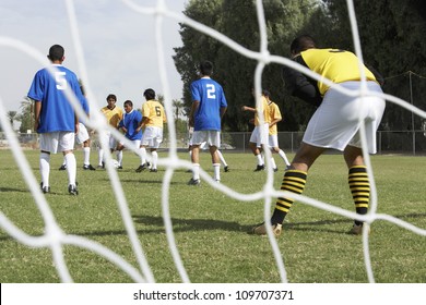 Goalkeeper ready to save a shot with players running with the ball in the background - Powered by Shutterstock