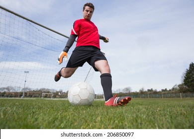 Goalkeeper in red kicking ball away from goal on a clear day - Powered by Shutterstock