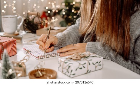 Goals plans make to do and wish list for new year christmas concept, girl writing in notebook. Woman hand holding pen on notepad at home on winter holidays xmas. Christmas decoration, gift boxes. 