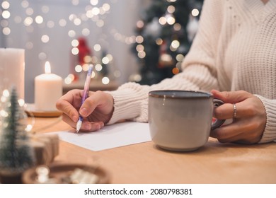 Goals plans make to do and wish list for new year christmas concept writing in notebook. Woman hand holding pen on notepad and coffee cup at home on winter holidays xmas.