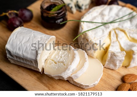Goat cheese with other cheese and jam in the background on a cut board