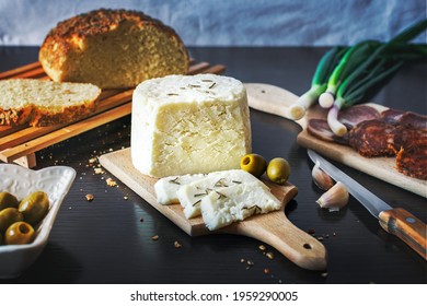 Goat cheese sliced on a wooden plate with freshly baked bread with green onions, smoked ham, sausage, olives on a dark wooden dining table.Top view - Powered by Shutterstock