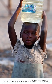 GOBABIS/BOTSWANA - APRL 01, 2016: Unknown girl in her village in Botswana. She is carrying a water-filled canister on her head. She has taken the water from the well. Her skin and clothing is dusty.