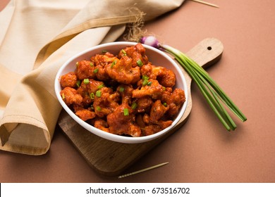 Gobi Manchurian dry - Popular street food of India made of cauliflower florets served in a white bowl or wooden plate, selective focus