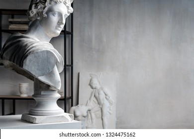 God Apollo bust sculpture. Ancient Greek god of Sun and Poetry Plaster copy of a marble statue on grange concrete wall background in studio. Copyspace for text.