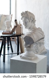 God Apollo Bust Sculpture. Ancient Greek God Of Sun And Poetry Plaster Copy Of A Marble Statue On Grange Concrete Wall Background In Studio. Copyspace For Text