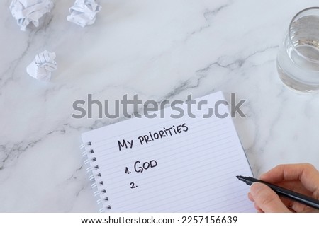 God first, top priorities list, handwritten text on a spiral notebook with human hand holding black marker. Seek first His Kingdom and righteousness, Christian biblical concept, top view.