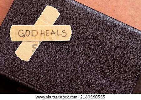 God heals, a handwritten message text on a bandage tape with closed Holy Bible Book with copy space. Top view. Healing, salvation, restoration by Jesus Christ, Christian biblical concept.