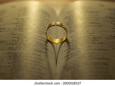 God Jesus Christ's blessing on the marriage relationship between husband and wife. Shiny golden engagement ring on open Holy Bible shadow forming heart. Faithful love, commitment, devotion, covenant.