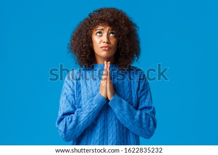 God please help find way. Supplicating faithful and hopeful young african-american woman in need, press hands together and pray looking up sky searching mercy or wayout, standing blue background