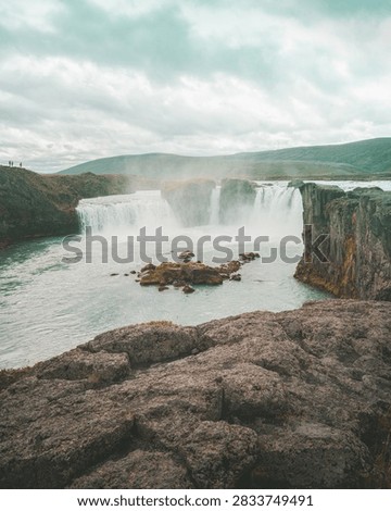 Godafoss waterfall cascading through a dramatic rocky landscape in northern Iceland beneath a cloudy sky.