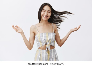 Goddess of natural beauty. Studio shot of carefree happy and emotive young female with hair floating on wind, speading raised hands asides and smiling broadly, enjoying windy and warm weather