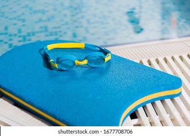Goggles On Flutter Board Near Swimming Pool With Blue Water