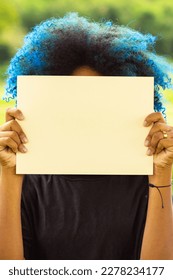 GOIANIA GOIAS BRAZIL - MARCH 20 2023: A young woman, with hair dyed blue, her face hidden behind a blank poster, with a landscape in the background.