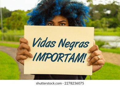 GOIANIA GOIAS BRAZIL - MARCH 20 2023: A young woman, with dyed blue hair, her face hidden behind a sign with the text: 