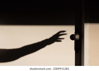 GOIANIA GOIAS BRAZIL - MAY 17 2023: The shadow of an arm with a hand trying to open a closed white door. - Powered by Shutterstock