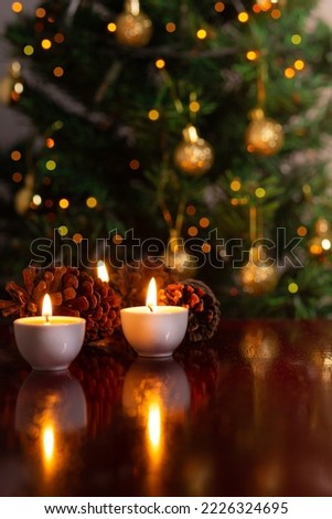 GOIÂNIA GOIAS BRAZIL – NOVEMBER 14 2022: Christmas decoration. Some lit candles on a reflective surface, and a defocused Christmas tree detail in the background.