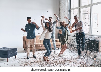 Gila. Penuh panjang bahagia orang-orang muda menari sambil menghabiskan waktu di rumah dengan confetti terbang di mana-mana