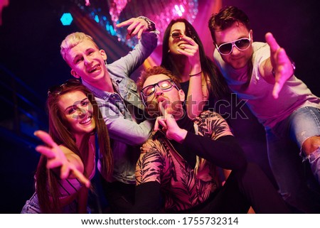 Going crazy and posing for the camera together. Young people is having fun in night club with colorful laser lights.