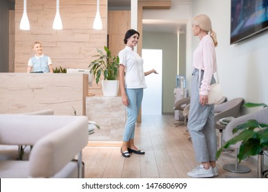 Going Healing Teeth. Smiling Dentist Standing In Front Of Her Patient Pointing At Her Office With The Hand Showing Her Where To Go.