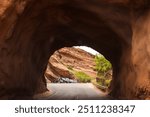 Going through the driving tunnel that was carved out of the Red Rocks at the famous Red Rock Amphitheater In Morrison Colorado USA with cars parked on the other side and some trees and shrubs