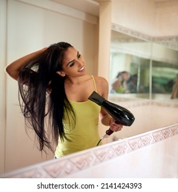 Going through her morning routine. Cropped shot of a young woman blowdrying her hair in the bathroom.