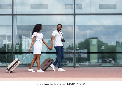 Going to travel. African couple walking with luggage near airport building, empty space