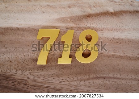 Gold Arabic numerals 718 on a dark brown to off-white wood pattern background.