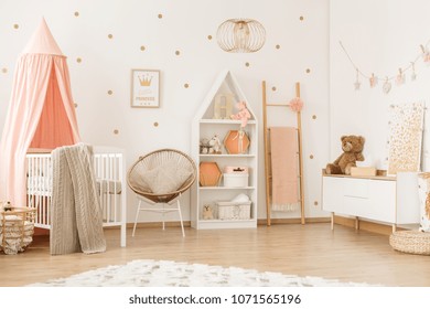 Gold armchair and ladder in pastel girly bedroom interior with canopied white crib