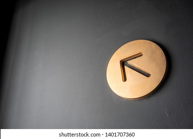 Gold arrow sign in circle shape frame  hanging against black wall for direction.