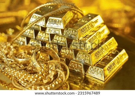 Gold bars and gold jewelry on the golden reflect light background. Gold is hard commodity good, risk asset, tangible value that used to be gold reserve,safe assets during war and   economic crisis.