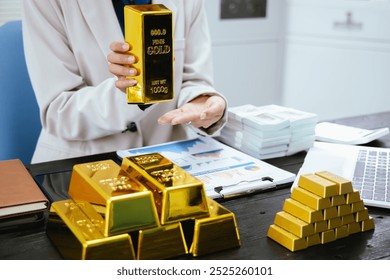 Gold bars and silver on table, Asian businesswoman at desk in office