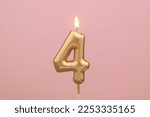 Gold birthday candle shaped as number 4 on pink background.