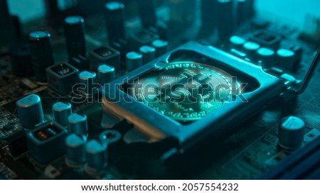 A gold Bitcoin coin with glare and reflection installed instead of a central processor in the motherboard with electronic components with blue light and smoke in the darkness. Bitcoin Mining