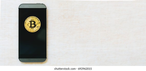 Gold bitcoin cryptocurrency with a smartphone on a wooden table - Shutterstock ID 692962015