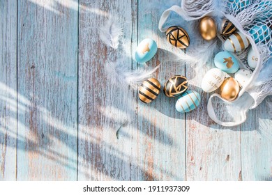 Gold, black, white, blue  eggs in a string bag on a blue wooden background. Geometry. The minimal concept. Top view. An Easter card with a copy of the place for the text. - Shutterstock ID 1911937309