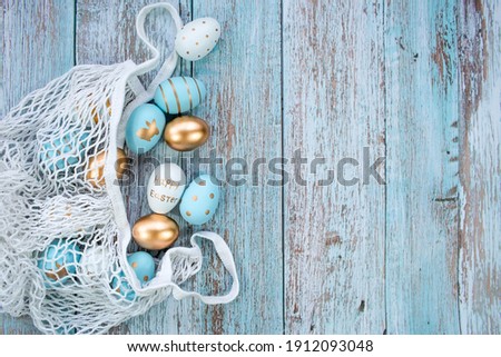 Gold, black, white, blue  eggs in a string bag on a blue wooden background. Geometry. The minimal concept. Top view. An Easter card with a copy of the place for the text.